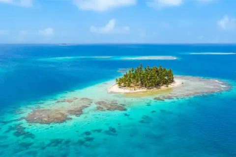 Una pequeña isla con palmeras, como la **isla bermeja**, emerge de aguas turquesas y azules, rodeada de arrecifes.