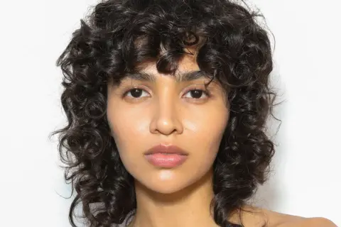 Volto di donna con capelli ricci scuri e un audace taglio capelli anni 80 mullet.