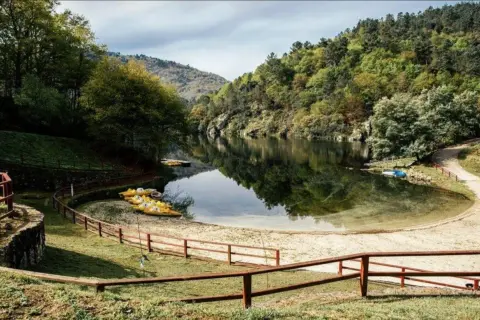 Un área de berres con botes amarillos esperando en la orilla arenosa, rodeada de exuberante vegetación y un lago tranquilo.