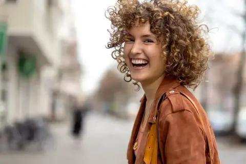Frau mit vollen, lockigen Haaren, die lacht. Perfekt gestylte Locken, die ihr Gesicht umrahmen.