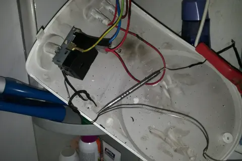Rozmontowany bojler z widocznym termostatem i przewodami. Jak sprawdzić termostat w bojlerze? To zdjęcie pokazuje wnętrze, gdzie znajduje się element grzewczy i okablowanie.