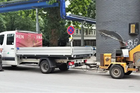 Ein Handwerker steht neben einem LKW mit Anhänger, der einen Holzhäcksler transportiert.