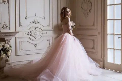 Kobieta w różowej sukni księżniczki z bukietem kwiatów w eleganckim wnętrzu.