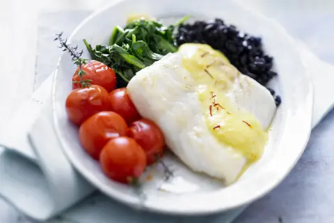 Filet de poisson blanc nappé de sauce safranée, accompagné de tomates cerises rôties, d'épinards et de riz noir. Une belle recette de turbot.