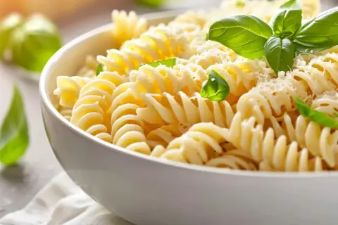 En skål med fusilli-pasta, toppad med riven ost och färsk basilika. Perfekt för ett snabbt pastasås recept.