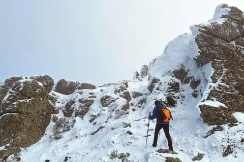 Un excursionista asciende una ladera nevada. Las rocas cubiertas de nieve forman una silueta que recuerda a una montaña con forma de mujer.