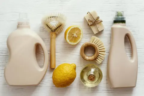 Dos botellas de detergente, jabón, limones y cepillos de madera para una limpieza sostenible.