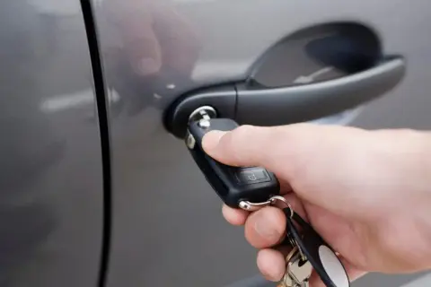 Dłoń z kluczykiem zbliża się do zamka w drzwiach samochodu.