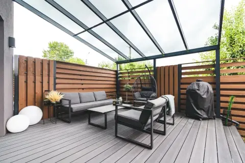 Arredamento moderno per un balcone con idee frangivista: divano, poltrone, dondolo e barbecue sotto una tettoia trasparente.