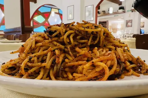 Un piatto di spaghetti con pomodoro e basilico, un classico del cibo barese, servito in un ristorante con vetrate colorate.