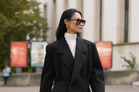 Stilvolles Outfit: Schwarzer Blazer über einem weißen Hemd mit Rollkragen kombinieren. Modische Sonnenbrille und goldene Ohrringe runden den Look ab.