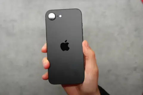 Czarna obudowa iPhone SE 4 z charakterystycznym jabłkiem Apple. Telefon trzymany w dłoni na szarym tle.