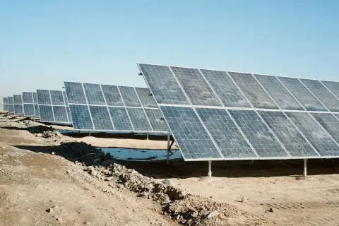 Fila de placas solares sucias bajo un cielo azul claro. La suciedad y el polvo cubren la superficie de los paneles, reduciendo su eficiencia.