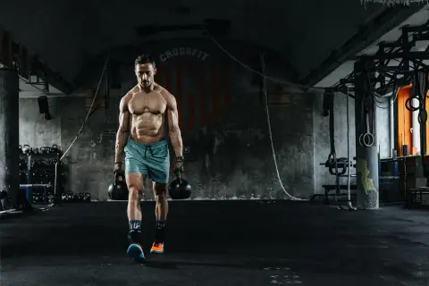 Mężczyzna z imponującą muskulaturą idzie z odważnikami w siłowni. To dowód, że crossfit dla kogo? Dla każdego, kto chce budować siłę i wytrzymałość!