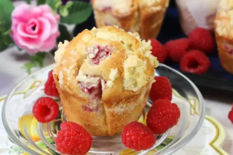 Pyszne muffinki z malinami, posypane kruszonką, otoczone świeżymi malinami.