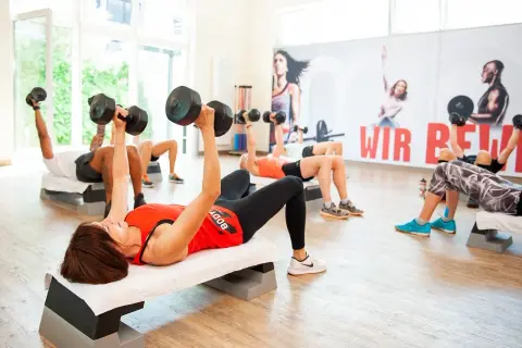 Ludzie ćwiczą z hantlami na ławkach. Czy cardio pomaga schudnąć? Tak, regularne ćwiczenia, jak te, wspierają redukcję wagi.