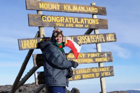 Zdobywca szczytu Kilimandżaro z polską flagą przy znaku "Uhuru Peak 5895m". Wyprawa na Kilimandżaro zakończona sukcesem!