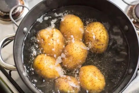 Mehrere Kartoffeln kochen in einem Topf mit sprudelndem Wasser. Sie sind fast gar, wenn sie leicht nachgeben.