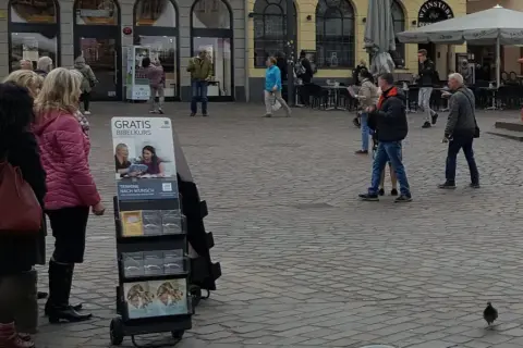 Zeugen Jehovas bieten einen kostenlosen Bibelkurs an. Menschen gehen vorbei, einige halten Broschüren in der Hand.