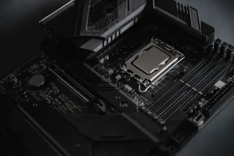 Czarna płyta główna z procesorem i slotami RAM. Widoczny radiator i elementy chipsetu.