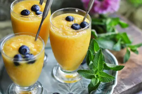 Tre glas med krämig mango smoothie, toppade med blåbär och mynta. En perfekt, uppfriskande dryck.