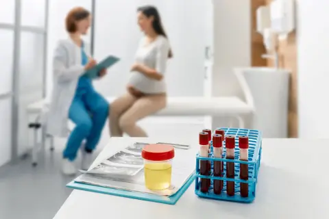 Badanie moczu w ciąży: obecność leukocytów może wskazywać na infekcję. Na stole próbka moczu, wyniki badań i probówki z krwią.