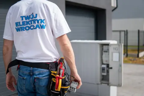 Elektryk z Wrocławia w pasie narzędziowym dokonuje odbioru instalacji elektrycznej. W ręku trzyma bezpiecznik.