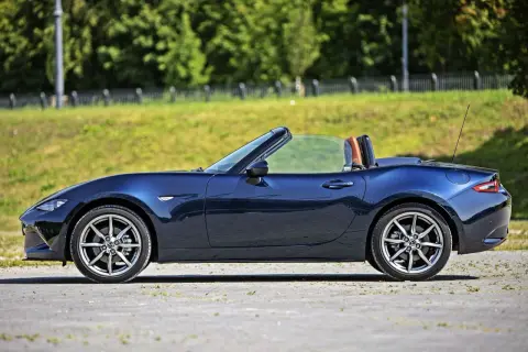 Granatowy roadster z otwartym dachem, gotowy na letnią przejażdżkę pośród zieleni.