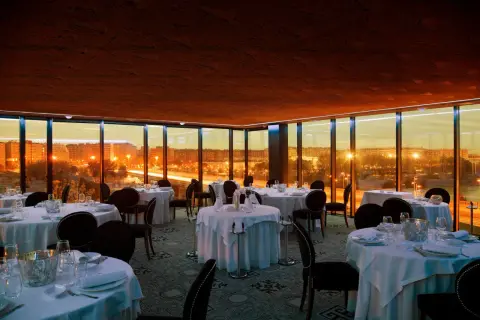 Elegante comedor con mesas puestas y vistas panorámicas de Zaragoza al atardecer. Un lugar perfecto para una cena especial en el rooftop.