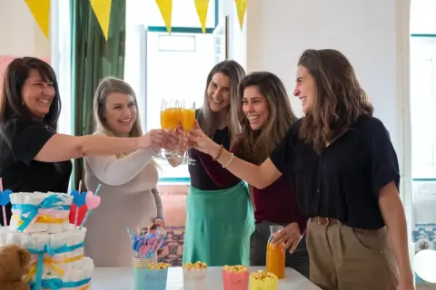 Przyjęcie baby shower: kobiety wznoszą toasty, przyszła mama w beżowym swetrze. Idealna stylizacja na baby shower to coś wygodnego i eleganckiego.
