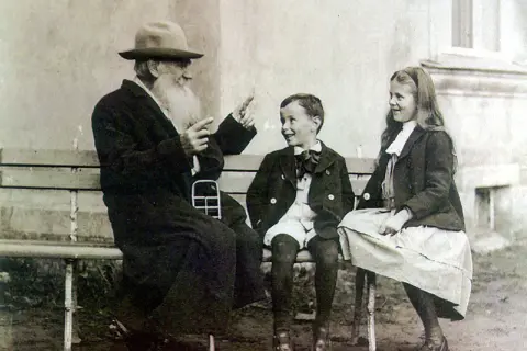 Lew Tołstoj w otoczeniu swoich dzieci, siedząc na ławce, opowiada im zapewne jakąś historię.