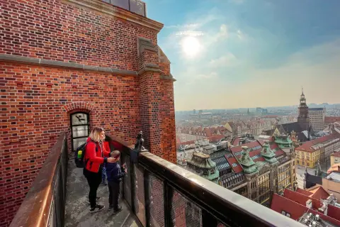 Kobieta z dzieckiem na moście pokutnic we Wrocławiu podziwia panoramę miasta.