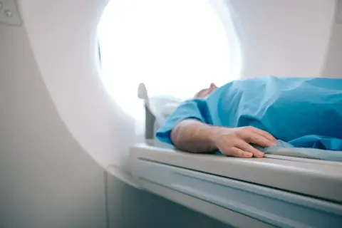 Pacjent w niebieskiej koszuli leży na stole rezonansu magnetycznego. Zastanawiasz się, ile kosztuje rezonans magnetyczny?