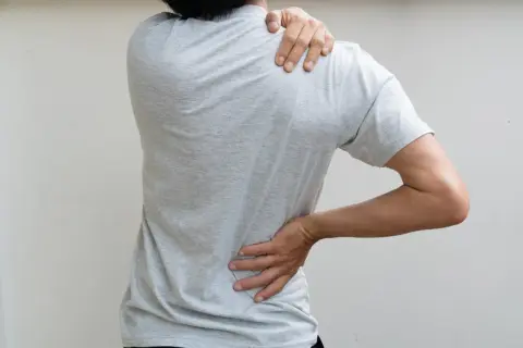 Person souffrant de dorsalgie, main sur l'épaule et le bas du dos. Recherche de traitement pour soulager la douleur.