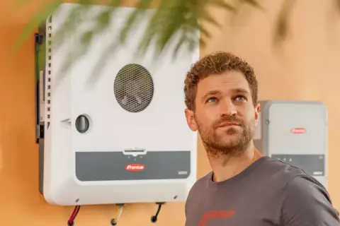 Hombre mirando hacia arriba junto a un inversor Fronius GEN24, símbolo de energía solar eficiente y sostenible.