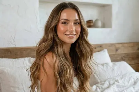 Mujer sonriente con cabello largo y ondulado, mostrando diferentes tipos de pelo con reflejos dorados.