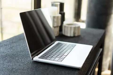 Nowy laptop czeka na pierwsze uruchomienie komputera. Na blacie obok stoją ozdobne świeczniki.