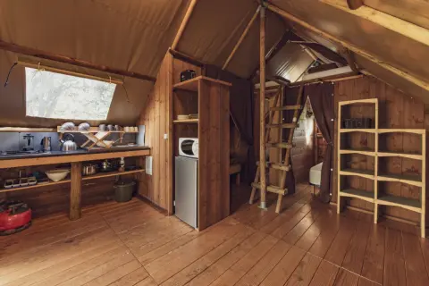 Intérieur d'une cabane en bois avec coin cuisine, réfrigérateur, étagères et échelle menant à un lit. Un havre de paix en Haute-Loire.