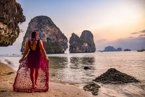 Kobieta w zwiewnej sukni spaceruje po plaży w Ao Nang, podziwiając skaliste wysepki o zachodzie słońca.