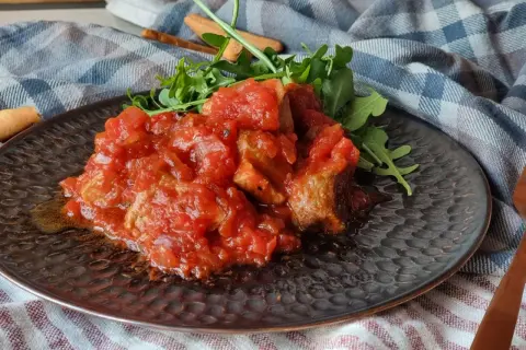 Magro con tomate, un plato casero con trozos de carne tierna bañados en una salsa de tomate casera, acompañado de rúcula fresca.
