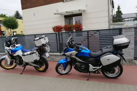 Dwa motocykle turystyczne z kuframi stoją przed nowoczesnym domem z kwiatami na balkonie.