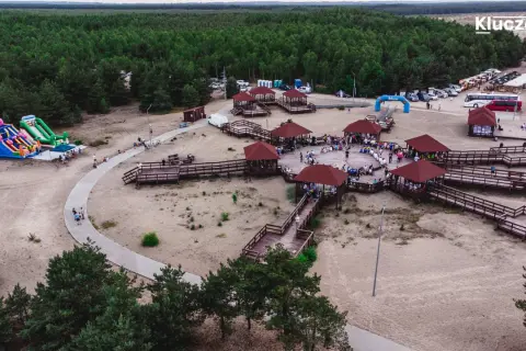 Drewniane zadaszone altany i ścieżki na piaszczystym terenie w miejscowości Klucze, otoczone lasem.