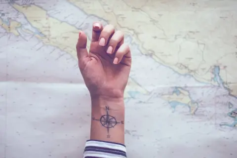 Ein feminines Kompass-Tattoo auf dem Handgelenk, bereit für das nächste Abenteuer auf der Seekarte.