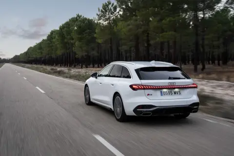 Białe Audi A5 Avant 2025 pędzi pustą drogą wśród sosnowego lasu.