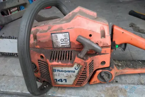 Pomarańczowa piła łańcuchowa Husqvarna 141, z widocznymi danymi technicznymi, gotowa do pracy.