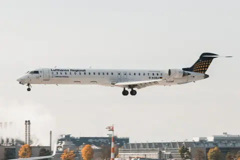 Samolot Lufthansa Regional z podwoziem wysuniętym do lądowania, leci nisko nad lotniskiem.