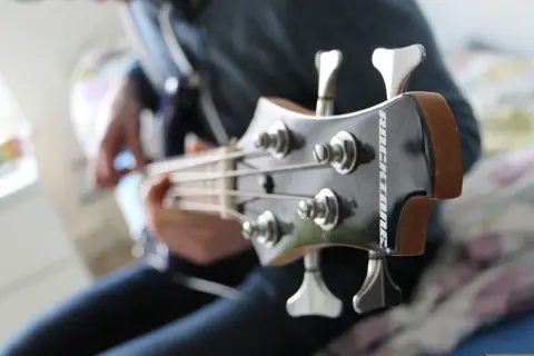 Osoba gra na gitarze basowej, wydobywając głębokie dźwięki na basie.