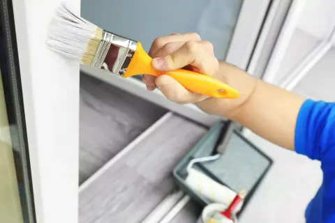 Hand streicht mit Pinsel weiße Farbe auf Kunststoffrahmen. Wetterfestes Ergebnis für Fenster und Türen.
