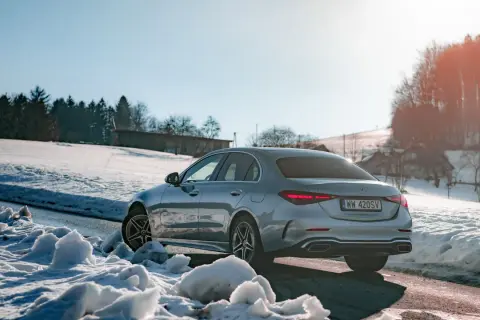 Srebrny Mercedes C 300 na tle ośnieżonych wzgórz i lasu. Zima nie straszna temu eleganckiemu autu.