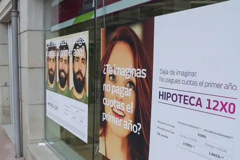 Anuncios de hipotecas en un escaparate. Uno muestra tres hombres y pregunta "¿Te imaginas no pagar cuotas el primer año?". Otro, con una mujer, dice "Deja de imaginar. No pagues cuotas el primer año. HIPOTECA 12X0". Se ve un **euribor forecast** en la ...